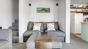 A modern living room with a grey sofa, a wooden coffee table, and a kitchen area with shelves and a refrigerator. - Great Location Corner Condo - Tamarack #10 Pets OK - 2 Bedroom Condo by Bear Valley Vacation Rentals (Arnold)