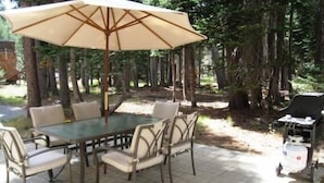 An outdoor dining area with a glass table and six chairs, surrounded by a large umbrella. - Great Location Corner Condo - Tamarack #10 Pets OK - 2 Bedroom Condo by Bear Valley Vacation Rentals (Arnold)