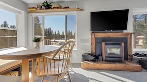A modern living room with a fireplace, a flat-screen TV, and a dining area with wooden furniture. - Great Location Corner Condo - Tamarack #10 Pets OK - 2 Bedroom Condo by Bear Valley Vacation Rentals (Arnold)