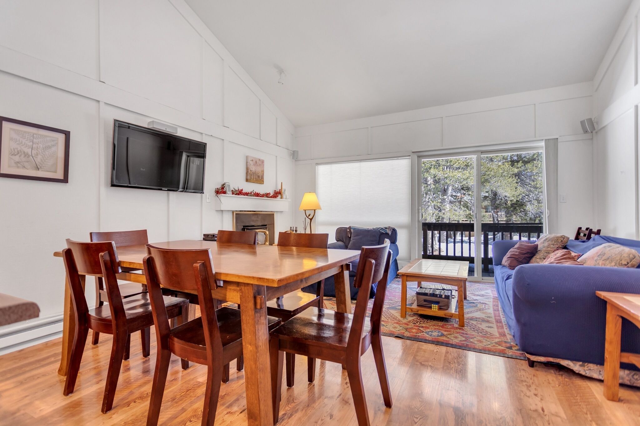 A modern living room with a wooden dining table, blue sofa, and a TV mounted on the wall.