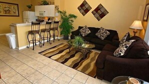 Un espace de vie compact comprenant un coin cuisine, une table à manger avec des chaises, un ensemble de canapés et un tapis à motifs.