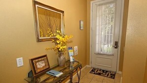 Un espace d’accueil avec une table en verre, un vase de fleurs jaunes, un tableau encadré et une porte dotée d’une fenêtre.