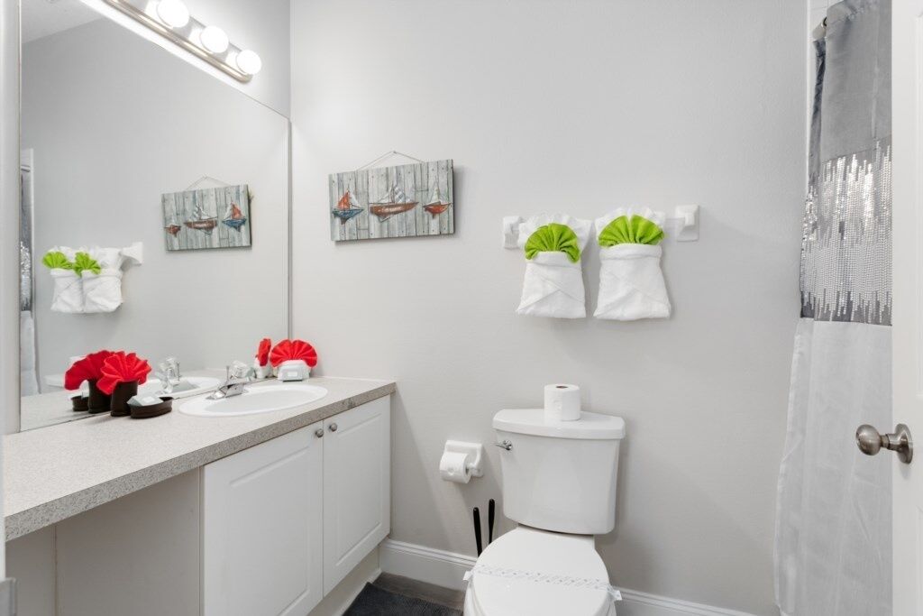 A bathroom with a sink, toilet, and shower curtain. There are towels hanging on the wall and a mirror above the sink.