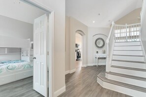 A spacious room with a bed, a white door, a staircase, and a hallway leading to a kitchen area. - Amazing 6 Bed Disney Dream Getaway In Windsor Palm 6 Bedroom Villa by RedAwning (Kissimmee)