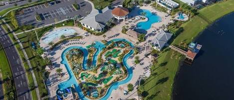 An aerial view of a resort with multiple swimming pools, a parking lot, and beachfront properties.