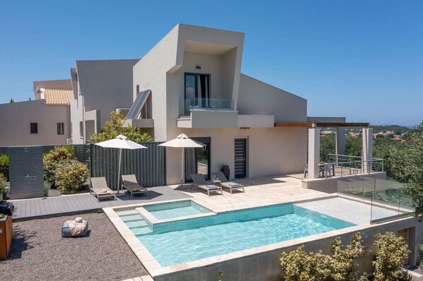 A modern two-story house with a swimming pool, outdoor seating, and a glass-enclosed balcony.