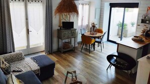 A modern living room with a sofa, ottoman, and a glass coffee table. There is a dining area with a table and chairs, and a kitchen area with a counter and cabinets. - Charming house la Rochelle easter vacations (La Rochelle)