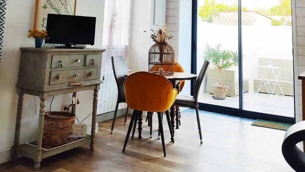 A modern living room with a large window, a dining area with orange chairs, and a rustic ceiling light. - Charming house la Rochelle easter vacations (La Rochelle)