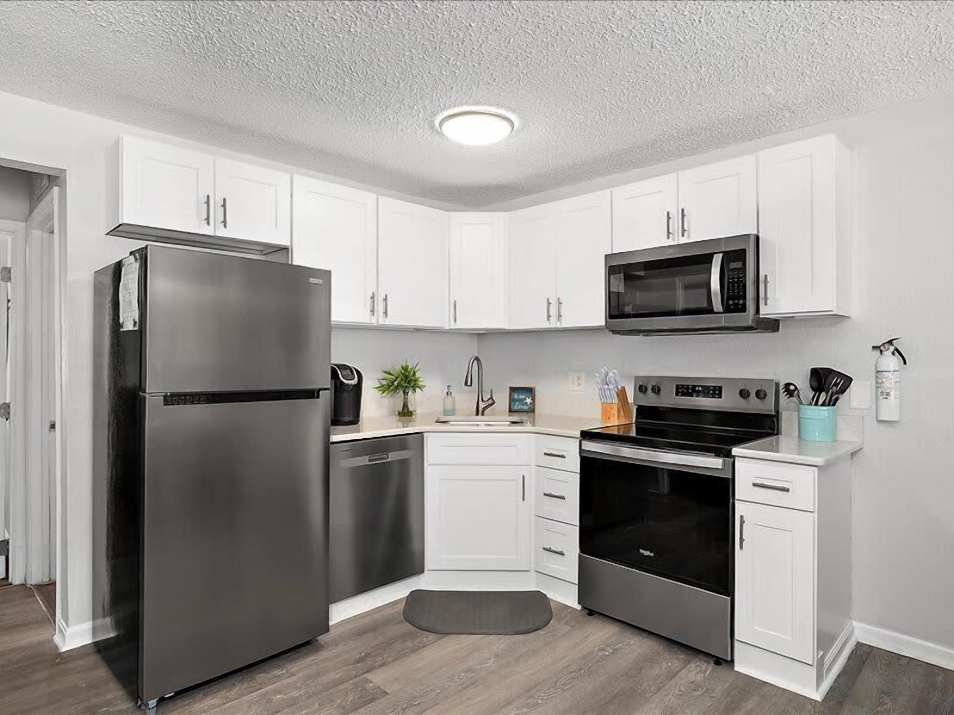 A kitchen with white cabinets, a stainless steel refrigerator, a microwave, an oven, and a dishwasher.