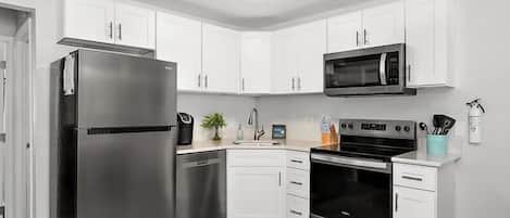 A kitchen with white cabinets, a stainless steel refrigerator, a microwave, an oven, and a dishwasher.