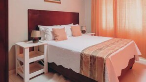 A neatly made bed with a white comforter and a patterned throw, flanked by two bedside tables with lamps, in a room with a wooden headboard and a framed picture on the wall.