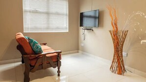 A room with a reclining chair, a television mounted on the wall, and a decorative vase.