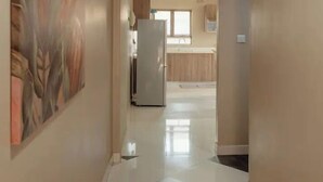 A hallway with a checkered floor, a large painting on the left, and a kitchen area in the distance.