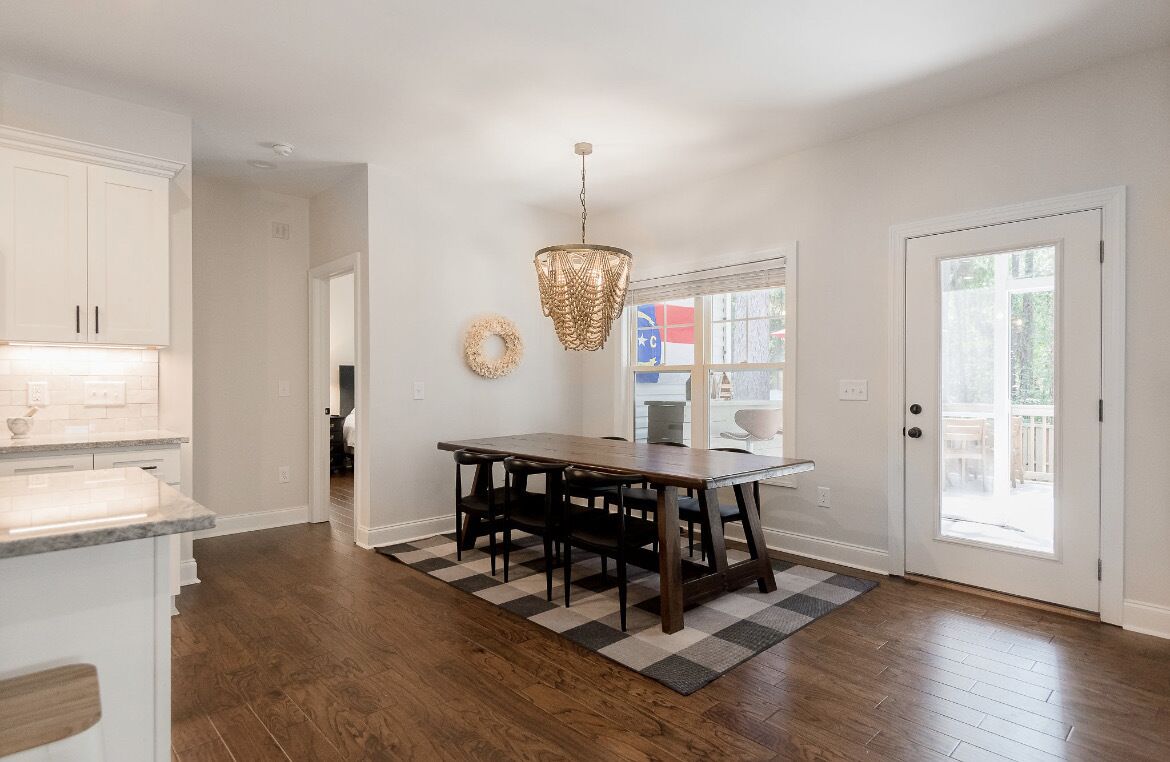 A kitchen with white cabinets, a wooden dining table, and a chandelier.