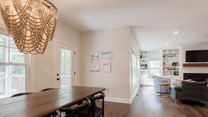 A spacious living area with a wooden dining table, a grey sofa, and a television mounted on the wall. - The 19th Hole: Sleeps 10. Pool Table, Fire Pit (Pinehurst)