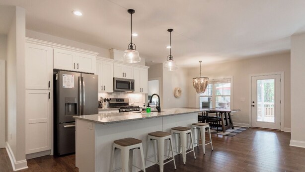 A modern kitchen with white cabinets, stainless steel appliances, a central island with bar stools, pendant lighting, and a view to the outside. - The 19th Hole: Sleeps 10. Pool Table, Fire Pit (Pinehurst)