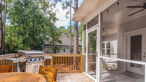 A wooden deck with a grill and table, surrounded by trees. - The 19th Hole: Sleeps 10. Pool Table, Fire Pit (Pinehurst)