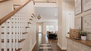 A staircase with wooden handrails and a checkered rug leading to a living area with a sofa and a coffee table. - The 19th Hole: Sleeps 10. Pool Table, Fire Pit (Pinehurst)
