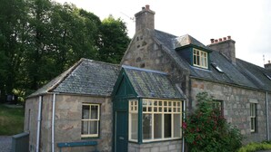 A stone building with a sloped roof, a small porch, and a bench.