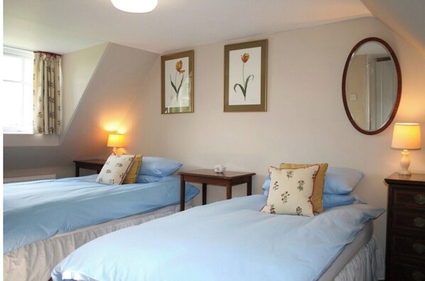 Une chambre avec deux lits, une petite table, un miroir et deux tableaux représentant des fleurs, accrochés au mur.