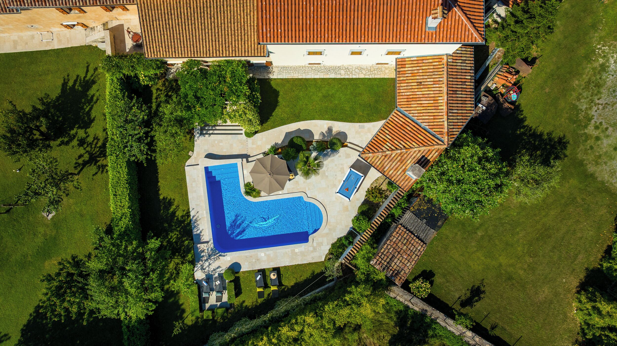 Oversigtsbillede af en ejendom med swimmingpool, overdækket terrasse og en indhegnet have.