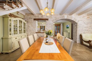 A dining room with a wooden table, chairs, a chandelier, stone walls, and a cabinet.