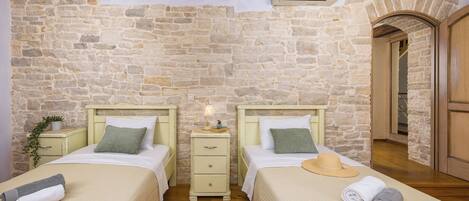 Une chambre avec deux lits, un mur en pierre, un plancher en bois, une table de chevet avec une lampe et un appareil de climatisation.
