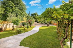 A garden pathway leading to a building with a stone wall and greenery.