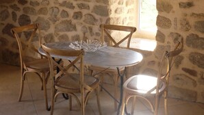 A stone-walled room with a round table and four wooden chairs.