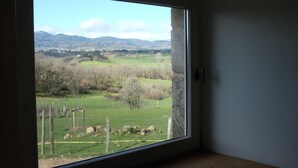 A room with a large window offering a view of a green field and distant mountains.