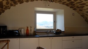 A kitchen with a stone ceiling, a window with a view of mountains, a sink, and cabinets.