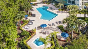 Vue aérienne d’un complexe hôtelier doté d’une grande piscine, de chaises longues et de palmiers.