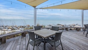Een overdekte buitenruimte met een tafel en stoelen, met uitzicht op een rotsachtige kustlijn.