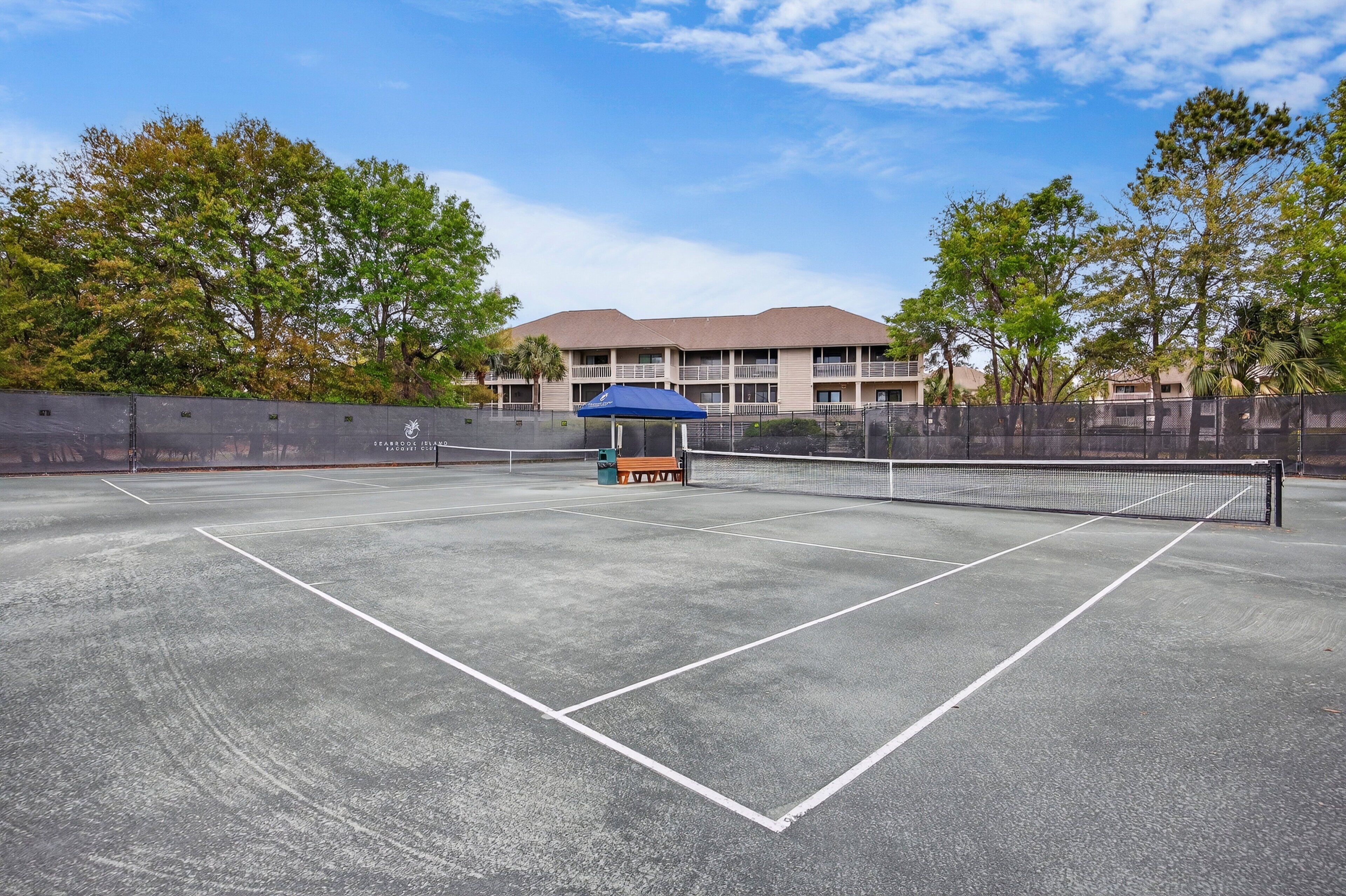 Una cancha de tenis con una red, una sombrilla azul y un edificio al fondo.