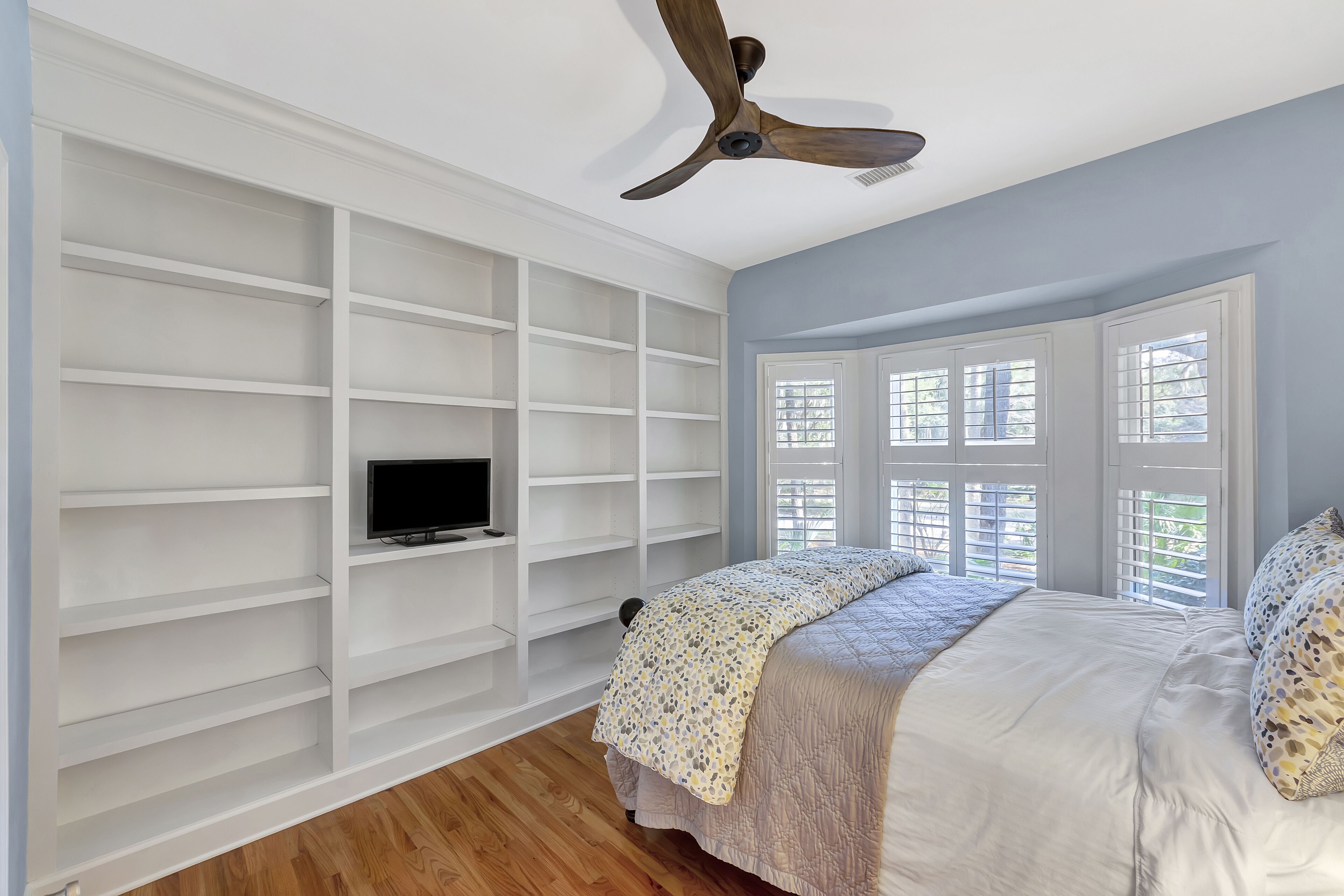 A bedroom with a bed, a TV on a shelf, and a ceiling fan.