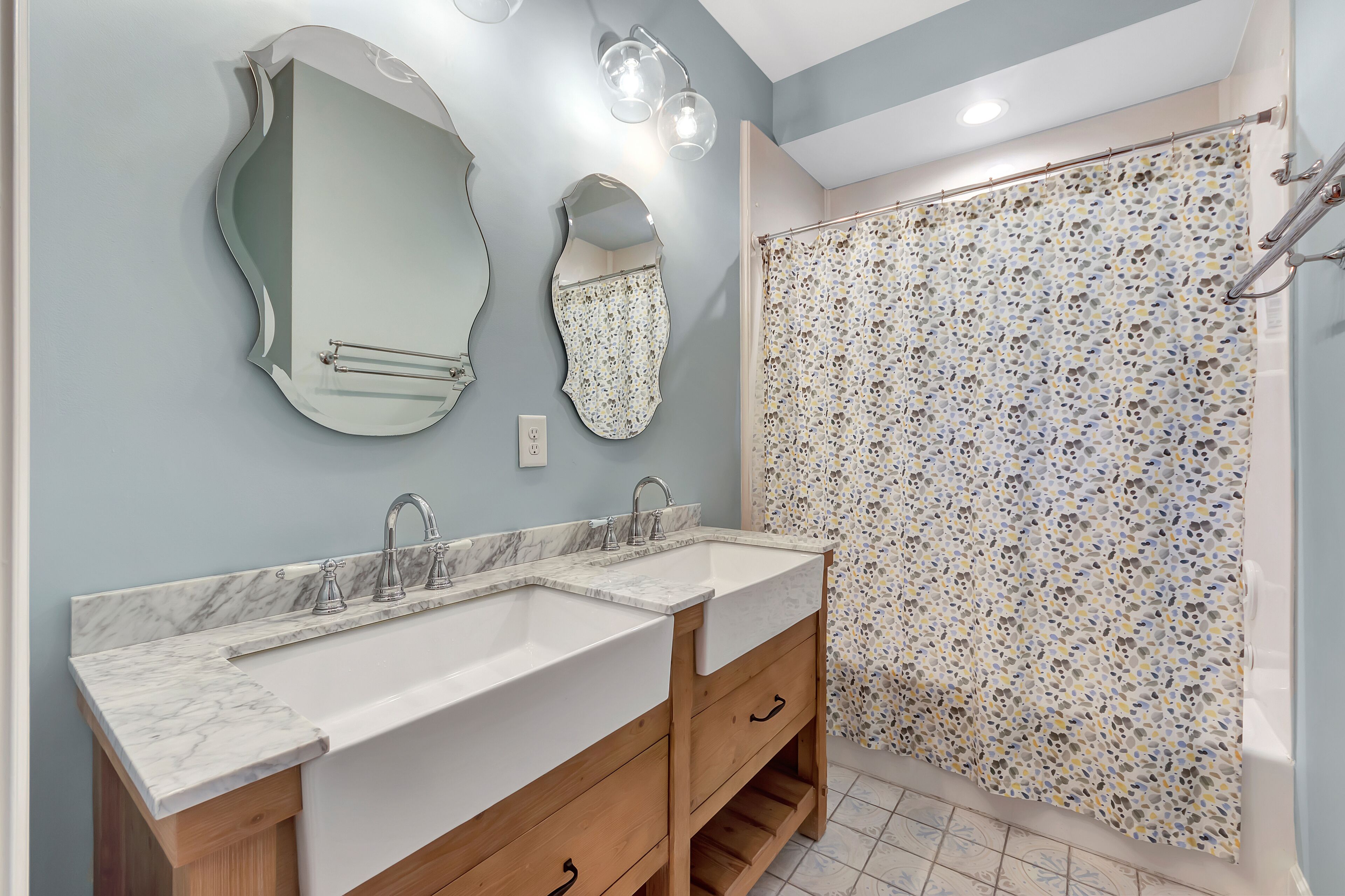 A bathroom with two sinks, wooden cabinets, and a shower with a mosaic tile wall.