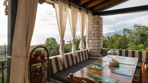 A wooden deck with a stone pillar, striped cushions, and a table with placemats. - Once Upon a Time - A Castle of Magical Sunsets (Kalamata)