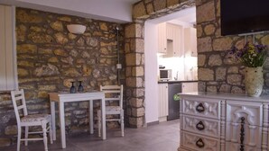 A room with a stone wall, a dining table with chairs, a white cabinet with drawers, and a television mounted on the wall. - Eleni's Coastal Retreat with Ocean View Gemstone (Kalamata)