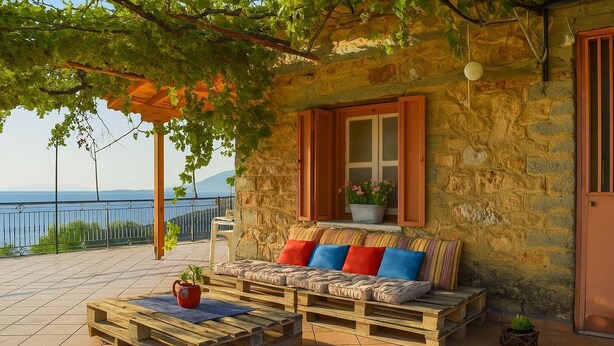 A cozy outdoor seating area with a stone wall, wooden bench, and a view of the sea. - Eleni's Coastal Retreat with Ocean View Gemstone (Kalamata)