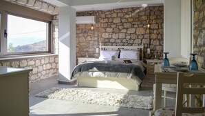 A bedroom with a stone wall, a bed with white linens, a desk with a chair, and a window with a view of the outdoors. - Eleni's Coastal Retreat with Ocean View Gemstone (Kalamata)