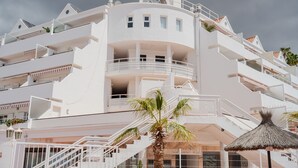 A multi-story white building with balconies, a palm tree, and a thatched roof structure. - Bungalow apartment with private pool & ocean views (Adeje)