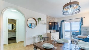 A dining area with a wooden table set for four, a TV mounted on the wall, and a view of the sea through the window. - Bungalow apartment with private pool & ocean views (Adeje)
