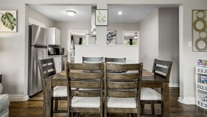 Un coin repas avec une table et des chaises en bois, un réfrigérateur et un four à micro-ondes en arrière-plan.