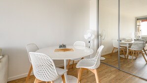 A modern dining area with a round white table, white chairs with wooden legs, and a large mirror reflecting the room. - Bright Apt With Balcony And Sea View (Antibes)