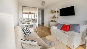 A modern living room with a white sofa, a round coffee table, and a flat-screen TV mounted on the wall. - Bright Apt With Balcony And Sea View (Antibes)
