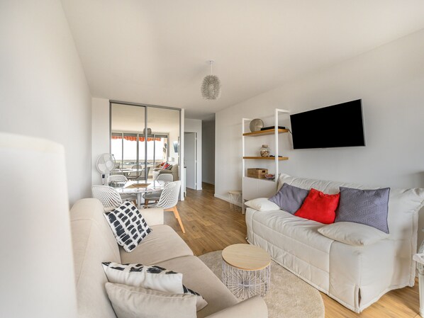 A modern living room with a white sofa, a round coffee table, and a flat-screen TV mounted on the wall.