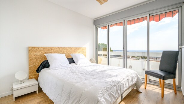 A bedroom with a large bed, a nightstand, a chair, and a ceiling fan. - Bright Apt With Balcony And Sea View (Antibes)