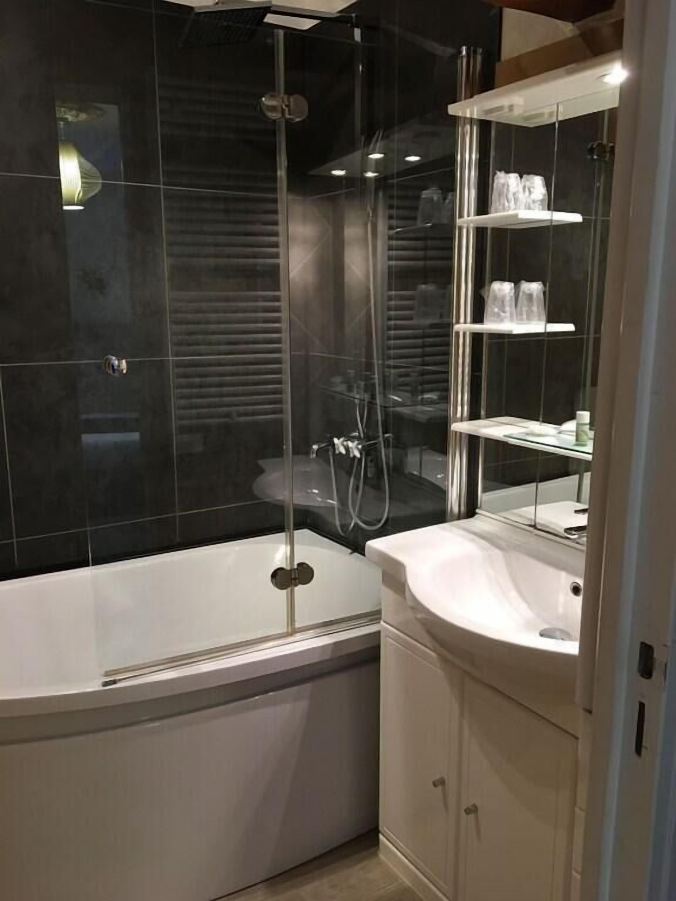 A modern bathroom with a glass-enclosed shower, a white bathtub, and a vanity with a mirror.