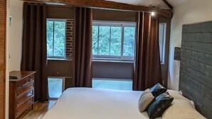 Quarto com cama grande, vigas de madeira, cômoda e janela com cortinas.