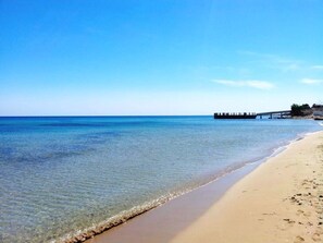 A beach with clear water, a sandy shore, and a pier extending into the water.